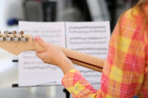 Female hand holding wooden neck of electric guitar